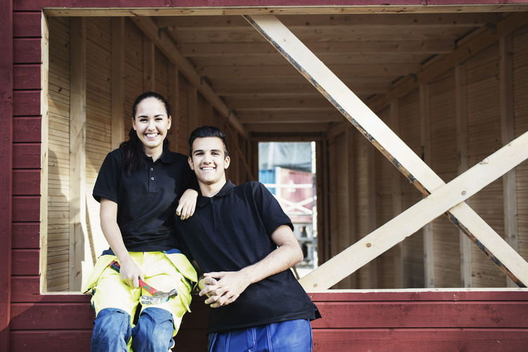 Portrait of happy carpentry students outside wooden cabin