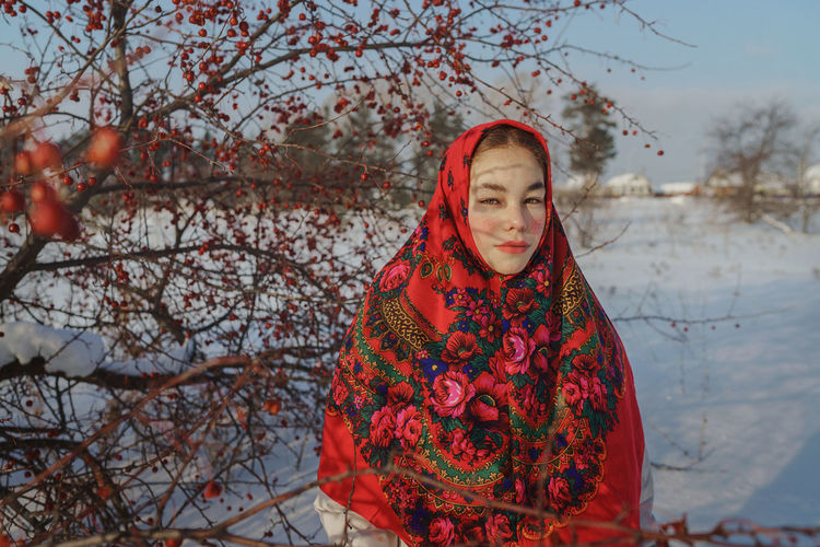 Woman standing by tree during winter in red shawl
