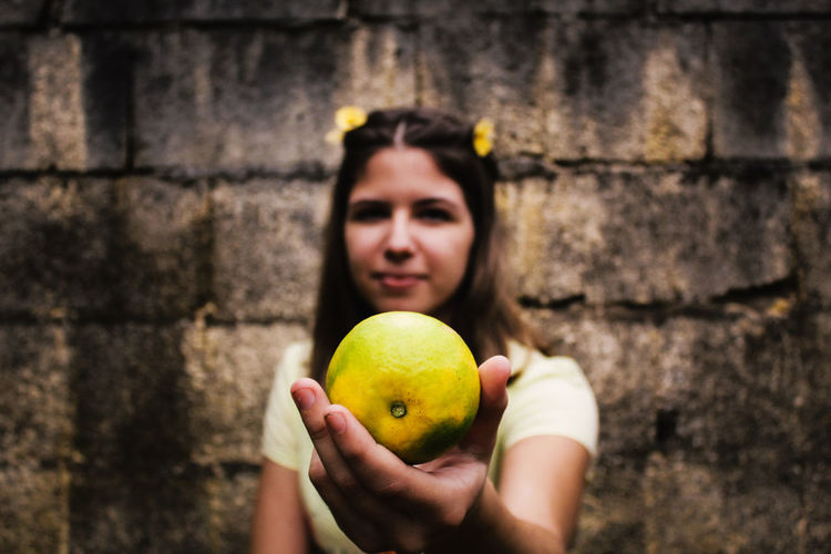 Young woman holding orange fruit against wall