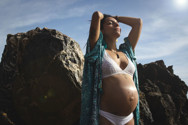 Pregnant young woman standing on rock against sky