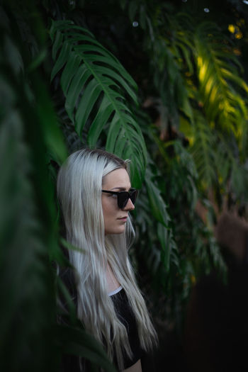 Young woman wearing sunglasses while standing against tree