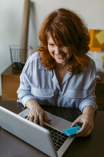 Smiling woman doing online shopping on laptop while sitting at home
