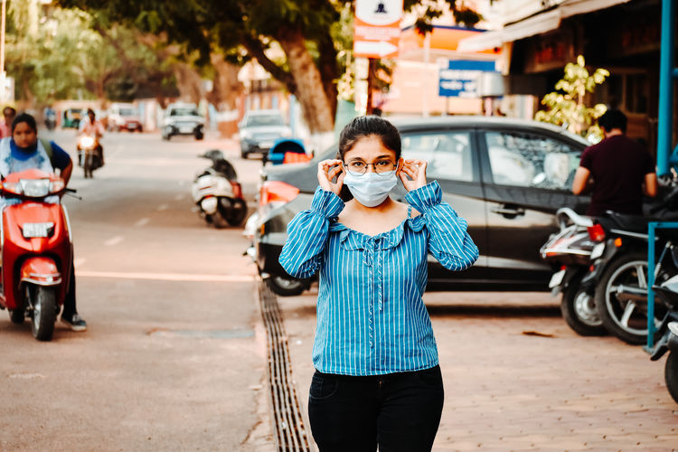 Woman wearing mask while standing on sidewalk in city