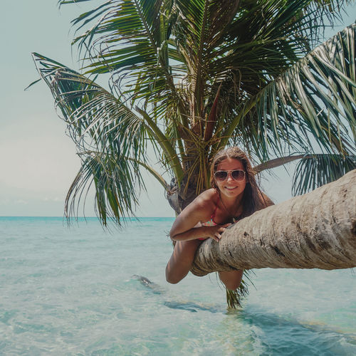 Portrait of smiling woman on palm tree over sea