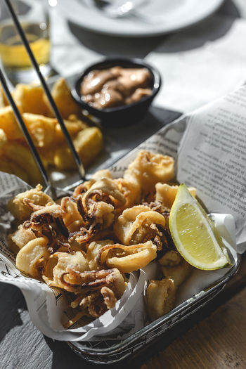 From above of fried small octopuses served in fryer basket with slice of lemon on festive table in restaurant