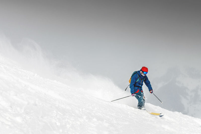 Skiing, skier, frisky - freeride, a man is stylishly skiing on a snowy slope with snow dust plume