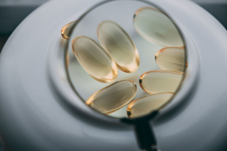 Yellow transparent omega 3 capsules under a magnifying glass. drug development concept