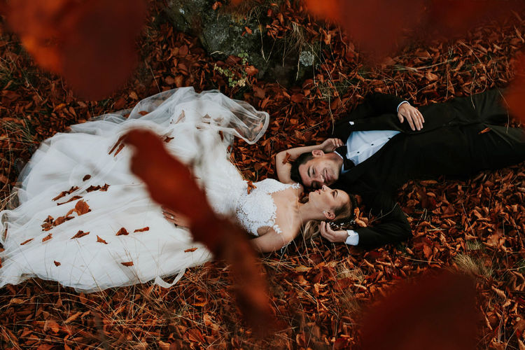 High angle view of wedding couple lying on dry leaves in park during autumn