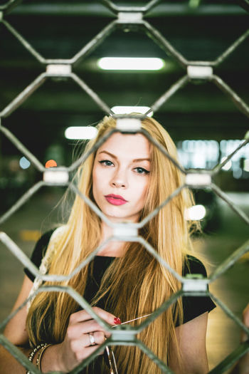 Portrait of young woman standing at parking garage seen through fence