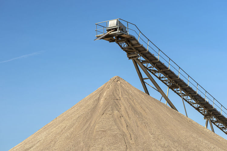 Conveyor belt over heaps of gravel against the blue sky at an industrial cement plant.