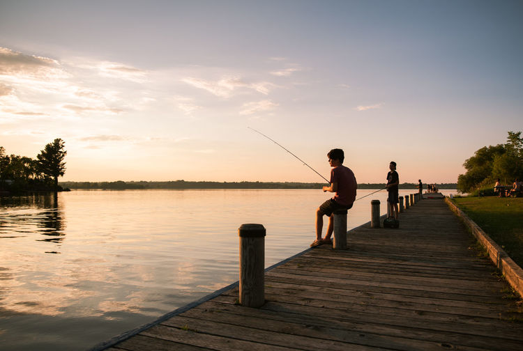 Man fishing on pier against lake during sunset