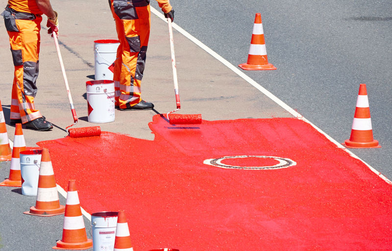 Workers carrying out marking work on a road that is marked with red paint