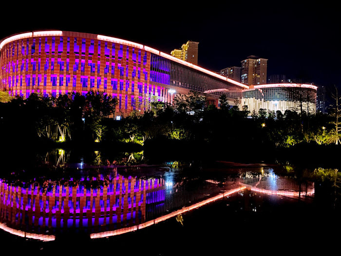 Illuminated ferris wheel by river at night