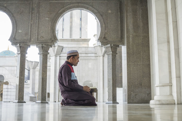 Side view of mature man reading koran while kneeling at mosque