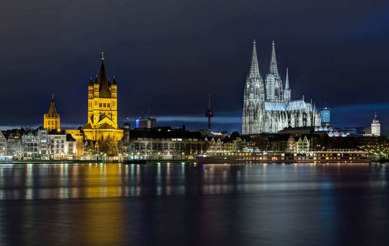 Illuminated buildings and cologne cathedral by rhine river in city at night
