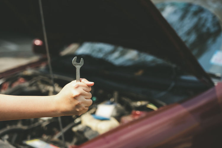 Cropped hand of woman holding wrench while repairing car