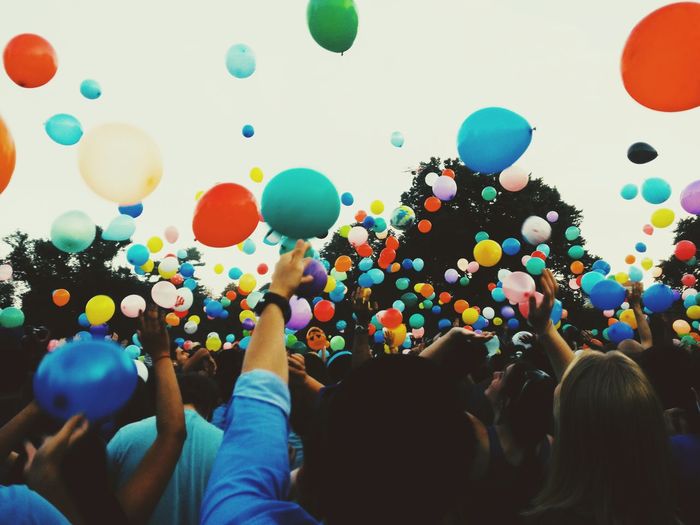 Crowd throwing colorful balloons against sky during festival