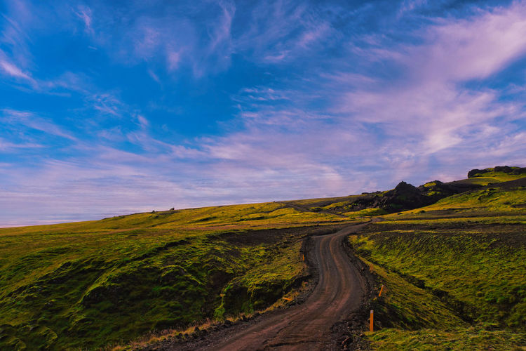 Dirt road amidst landscape against sky