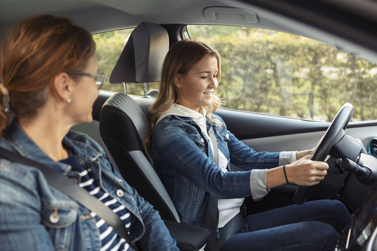 Mother teaching smiling teenage girl driving during weekend
