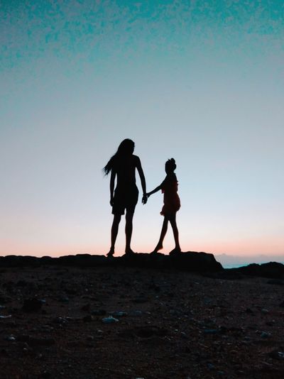 Silhouette friends standing on street against sky during sunset