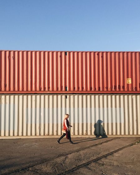 Full length of woman walking against cargo container during sunny day