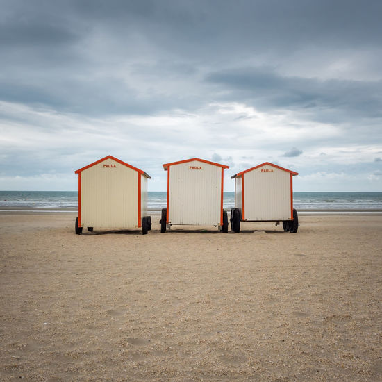 Three beach huts against cloudy sky