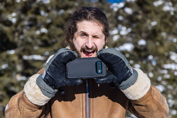 Portrait of man photographing with smart phone in winter