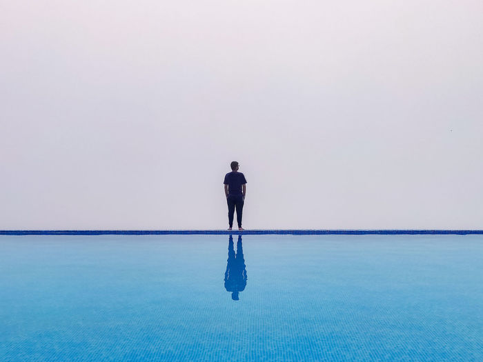 Rear view of standing by infinity pool against sky