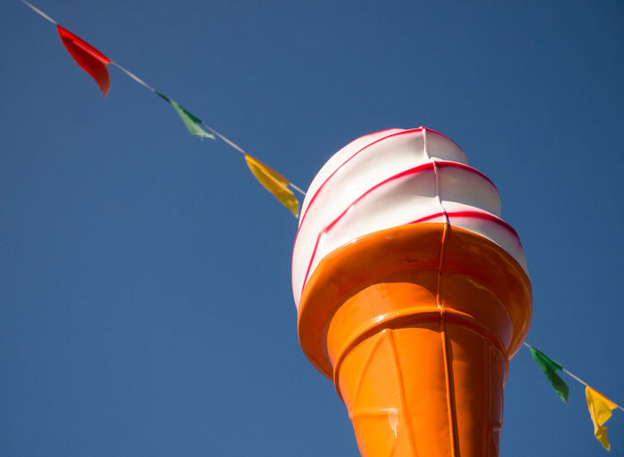 Ice cream cone statue, with multi coloured flag bunting and a clear blue sky behind