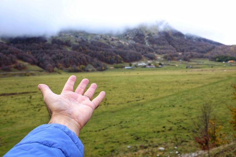 Close-up of hand on field against sky