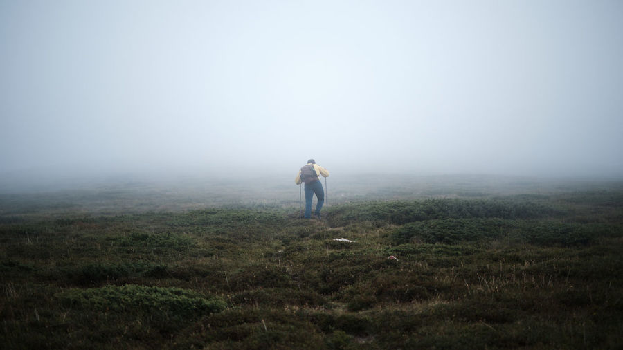 Full length rear view of man hiking on a steep mountain in fog