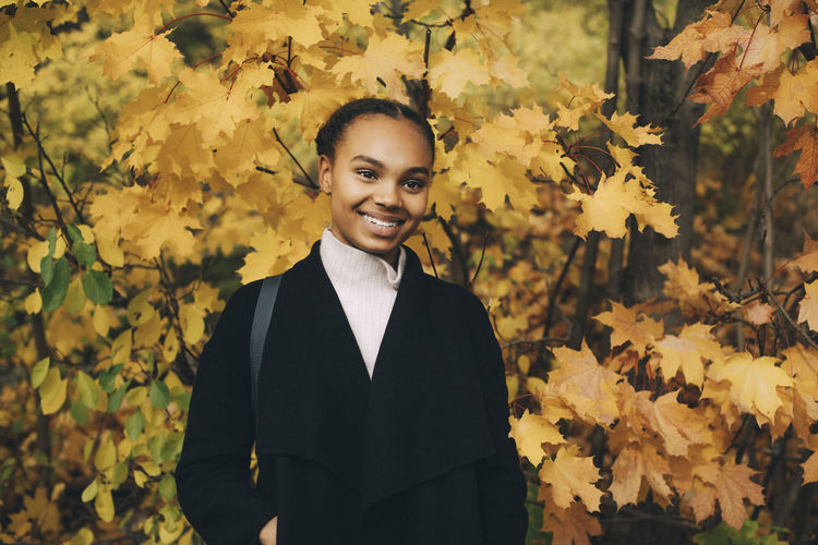 Portrait of smiling young woman standing by leaves during autumn