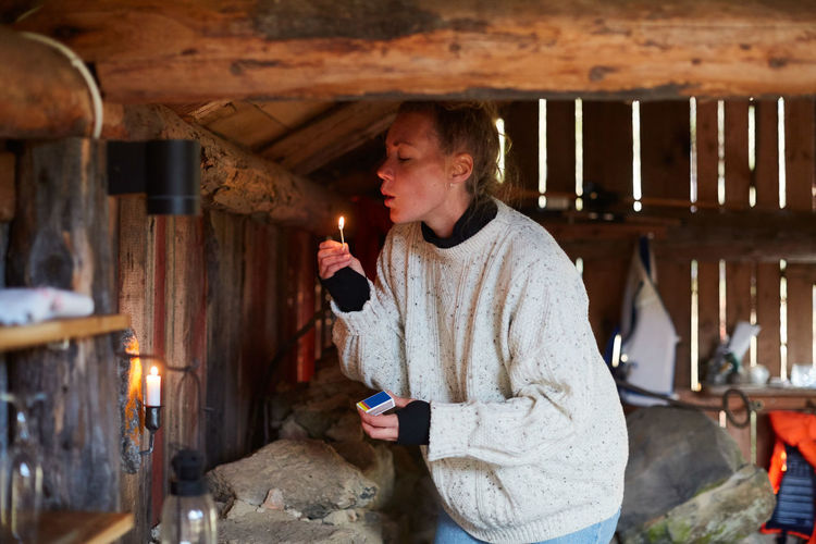 Mid adult woman blowing matchstick while standing in cottage