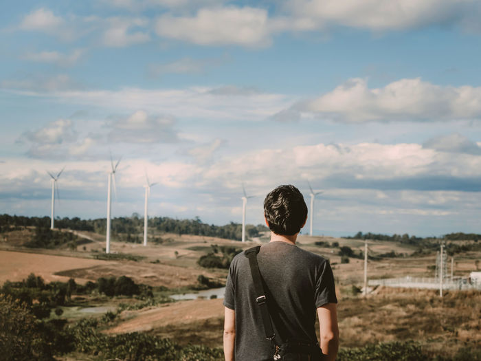 Asian man travel stand pose and see to sky for wait his girlfriend with wind turbine background