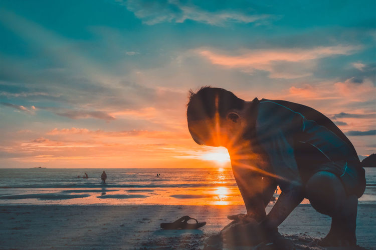 A boy playing on the beach against sunset sky