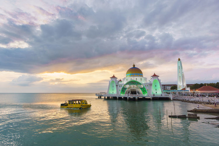 Mosque by sea against cloudy sky