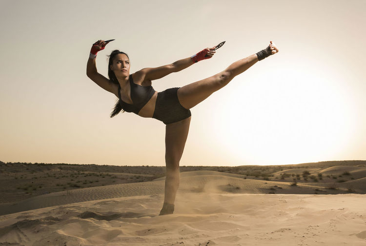 Full length of young woman standing on sand dune against clear sky