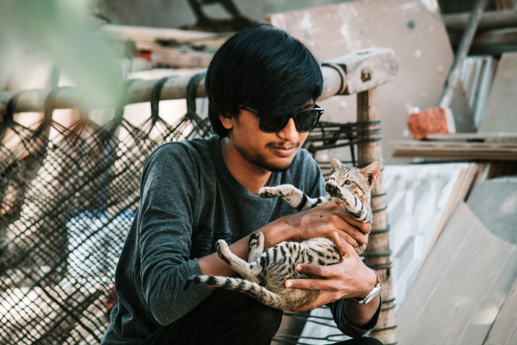 Young man holding cat while crouching outdoors
