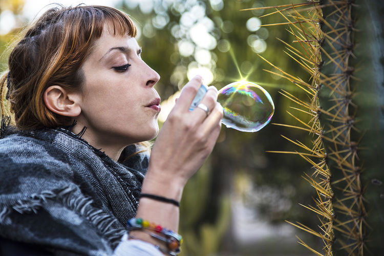 Profile view of woman blowing bubble by cactus
