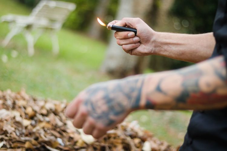 Midsection of man with tattooed hand holding lit cigarette lighter