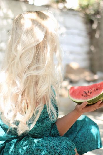 Rear view of woman holding watermelon outdoors