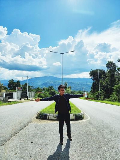Full length of young man standing on road against sky