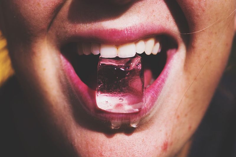Cropped image of woman holding ice in mouth