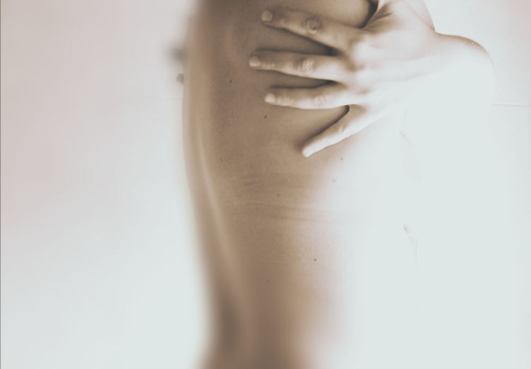 Midsection of topless young woman hugging self against white background