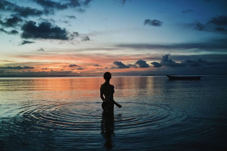 Rear view of woman standing in rippled sea during sunset
