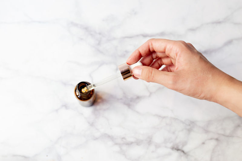 Top view of hand holding a retinol oil serum pipette and oil bottle 