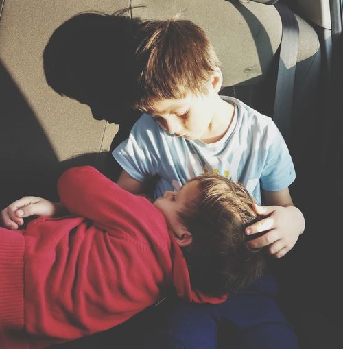 Cute boy looking at brother sleeping on lap while sitting in car