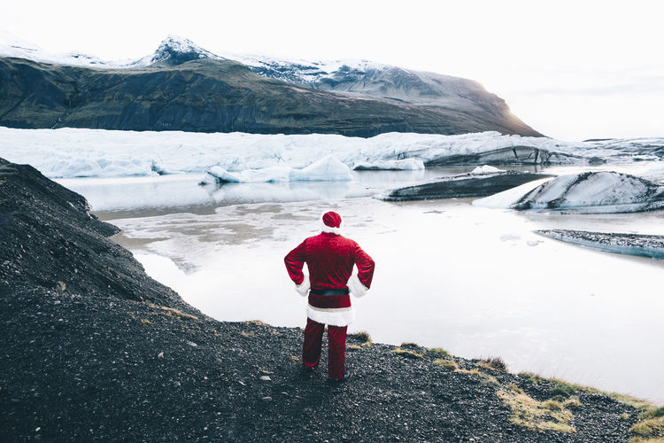 Rear view of man wearing santa claus costume looking at lake during winter