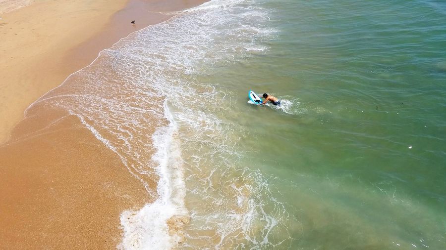 High angle view of shirtless man surfing board in sea