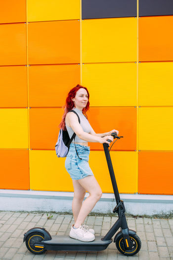 Young bright woman smiles and rides an electric scooter in the summer in city